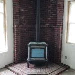 wood burning fireplace in corner lined with dark red brick